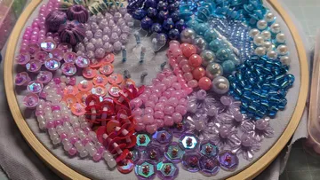 Colourful beads and sequins arranged in an embroidery frame.