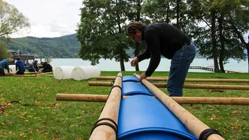 Person builds a structure out of wood and blue barrels.