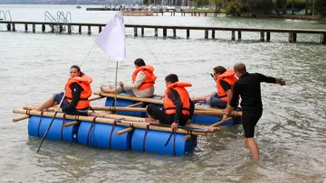 Five people sit in the water on a homemade raft.