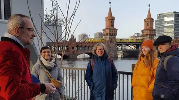 Gruppe von Personen hört einem Redner vor einer Brücke zu.