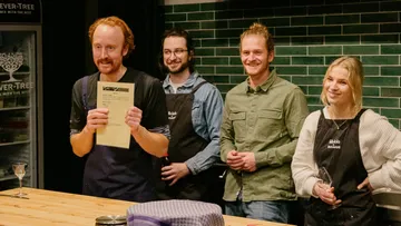 Four people are standing at a table and smiling.