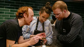 Three people cook together in a modern kitchen.