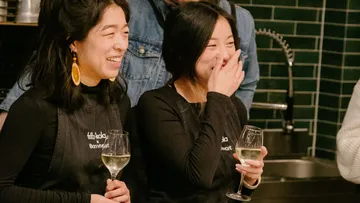 Zwei Frauen lachen und halten Weingläser in einer Küche.