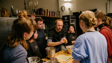 Koch zeigt Gruppe beim Zubereiten von Speisen in Küche.