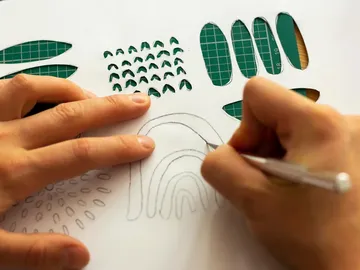 Hands draw designs on paper using stencils.