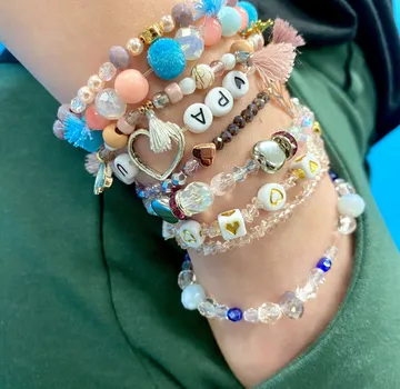 Bunte Armbänder schmücken einen Arm vor blauer Wand.