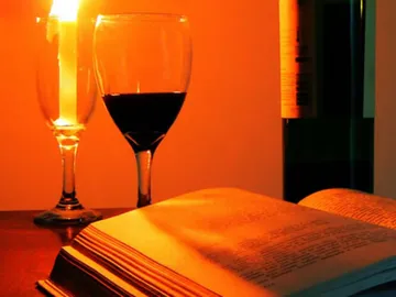 Kerze leuchtet neben einem Weinglas und aufgeschlagenem Buch.