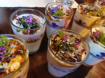 Gläser mit Schichtdesserts, dekoriert mit essbaren Blumen.
