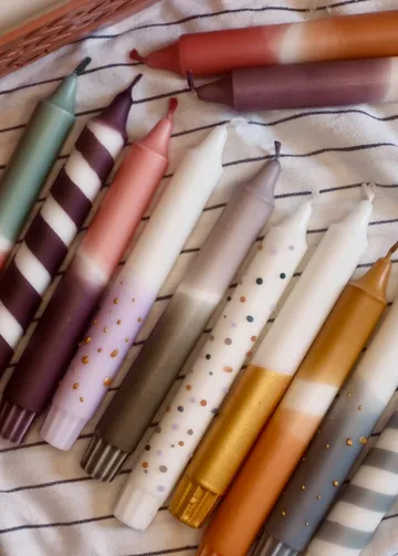 Bunte Kerzen liegen auf einem gestreiften Tuch.