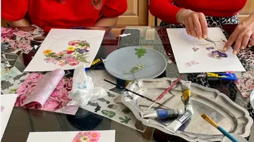Two people create illustrations with flowers on a table.