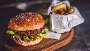Juicy burger with salad and fries on wooden board.