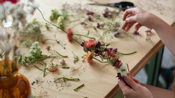 Blumen werden von Händen auf einem Holztisch arrangiert.