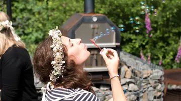 Woman blowing soap bubbles in garden surrounded by plants.
