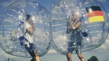 Two people in transparent balls bump into meadow.