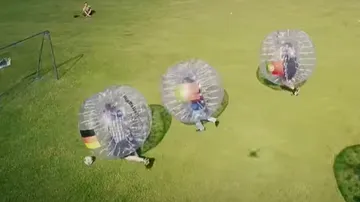 Players in air balls run across a soccer field.