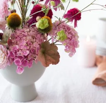 Bunte Blumen in einer grauen Vase auf einem Tisch.