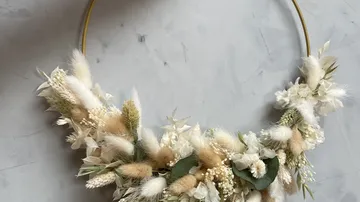 Wreath of flowers hangs decoratively on a wall made of plant material.