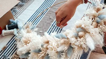 A hand creates a wreath of dried flowers.