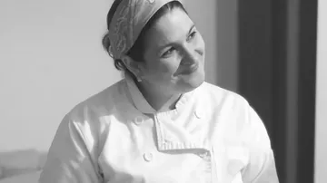 Chef in white uniform smiles in a bright room.