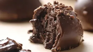 Chocolate praline, broken open, shows creamy filling, on wood.