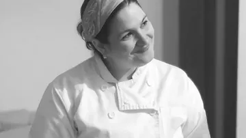 Chef smiles as she stands in a kitchen.