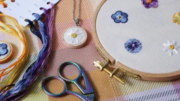 Stickrahmen mit Blumenstickerei, umgeben von Garn und Scheren.