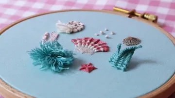 Gestickte Muscheln und Korallen auf blauem Stoff.