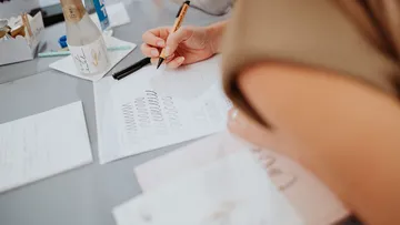 Hand schreibt auf einem Blatt Papier, umgeben von Materialien.