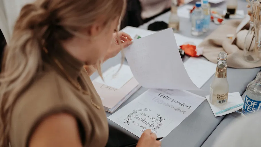 Frau hält ein Blatt Papier und schreibt an einem Tisch.