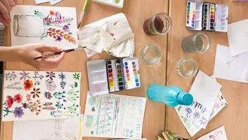 Buntes Zeichnen auf Tisch mit Aquarellfarben und Papiere.