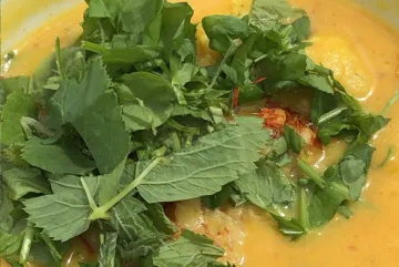 Grünes Gemüse liegt auf gelber, cremiger Suppe.