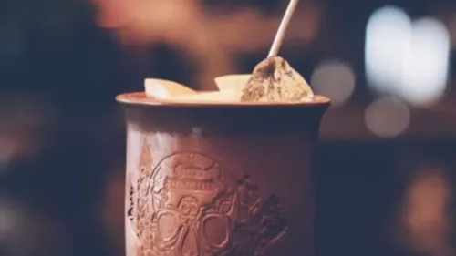 Clay cup with drink decorated with wooden skewer and fruit.
