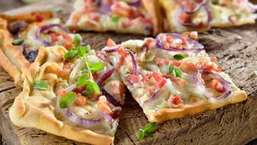 Flammkuchen with onions and bacon is on a wooden board.