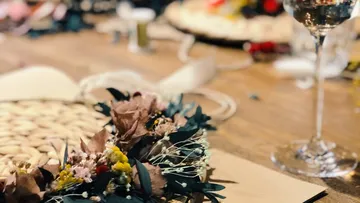 Blumenkranz liegt auf einem Tisch, Gläser im Hintergrund.
