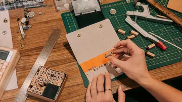 Hands stamp letters on card, redesigned at the table.