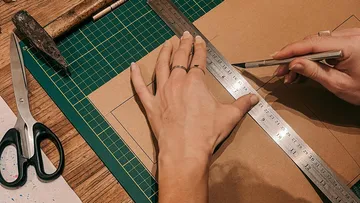 A hand cuts cardboard on a table with a cutter.