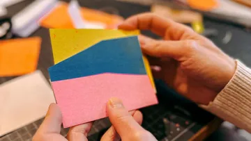 Bunte Papiere werden in den Händen gehalten und betrachtet.