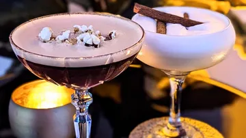 Two cocktails are sitting on a candlelit table.