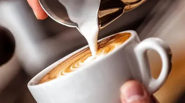 Milchschaum wird in eine Tasse Kaffee gegossen.