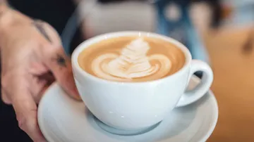 Cup of coffee with foam design is held by hand