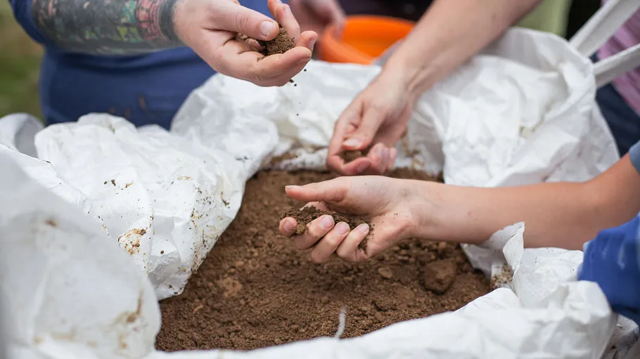 Hands grab soil from a large container.