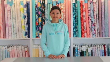 Woman standing smiling in front of colorful rolls of fabric in the shop.