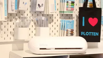 Schneideplotter auf Tisch, umgeben von Bastelmaterialien.