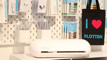 White plotter stands on a table surrounded by accessories.