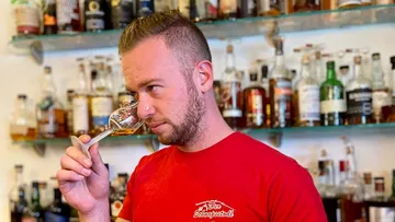 Ein Mann riecht Whisky in einem Glas vor einer Bar.