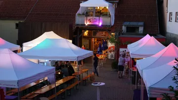 White party tents are set around tables in a lively setting.