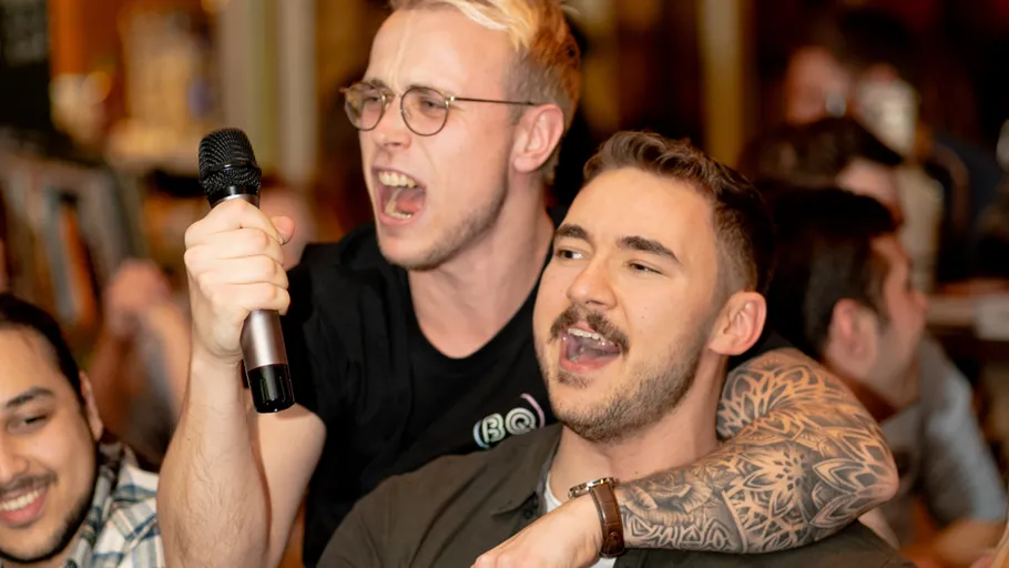 Two men sing enthusiastically in a lively bar.