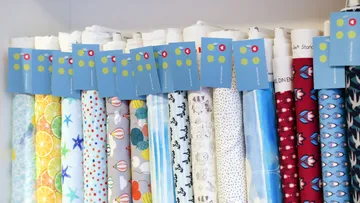 Colourful rolls of fabric are neatly placed on a shelf.
