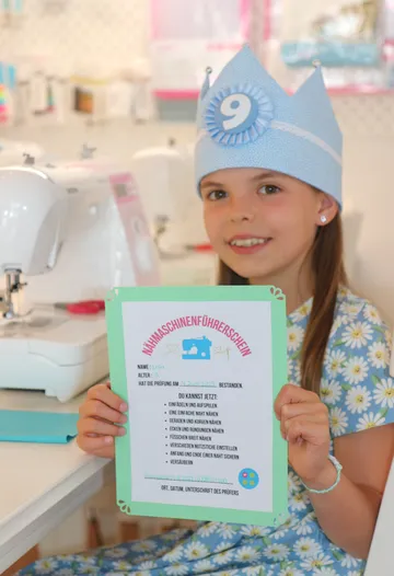 Girl holding sewing machine license in a bright room.
