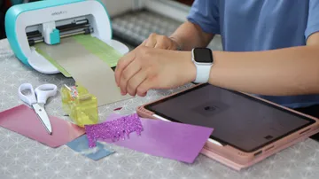 A person cuts craft materials with a machine at the table.